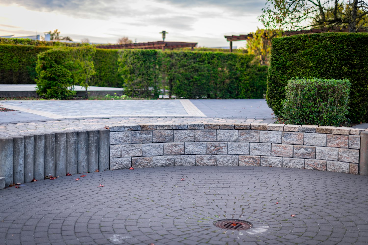 Runder Natursteinplatz mit geschwungener Mauer und Bepflanzung